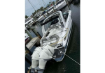 White motorboat docked at a marina, viewed from above, with a large Mercury outboard engine at the stern and a cushioned seating area inside.