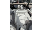 White boat cockpit with cushioned seating and a center hatch, docked at a marina with two outboard engines in the stern area.