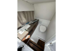 Small caravan bathroom with a sink, countertop, storage drawers, and a compact toilet; beige curtain along a window on the left.