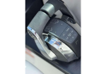 Close-up of a car steering wheel area with a multifunction control pad and glossy chrome trim, reflecting the photographer's image.