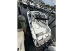 White motorboat docked at a marina, seen from above with cushioned seating and a cockpit area.