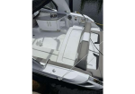 White motorboat cockpit with white and beige cushioned seating, steering console, and storage areas, docked on calm water.