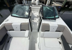 Top-down view of a white speedboat cockpit with two rear L-shaped cushioned seats, center aisle, and windshield panels, dock in the background.