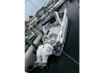 White motorboat docked at a marina, tied to a wooden dock with a large outboard engine at the stern and other boats moored nearby.