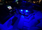Interior of a boat cockpit at night with blue LED lighting, steering wheel and navigation gauges visible beside plush seating.