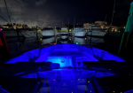 Night marina scene with several docked boats; blue LED lighting glows from a small speedboat in the foreground as reflections shimmer on the water