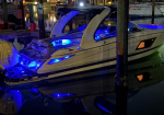 White motor yacht docked at a marina at night, blue deck and hull lighting reflecting on calm water, with open cockpit doors