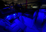 Blue-lit luxury boat interior at night showing seating, cupholders, and helm area with marina lights outside the windows.