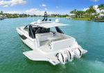 White speedboat docked in clear blue water with open rear deck and three outboard engines visible.