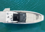 Top-down aerial view of a white motor yacht on bright turquoise water with a black-cabined cockpit area nearby.