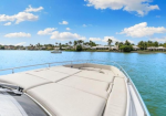 Front deck of a white motorboat on calm blue water with a shoreline of houses and palm trees in the distance.