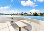 Luxurious white yacht deck with curved beige seating, a small table, and blue water ahead.