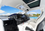 Luxurious white boat cockpit with black dashboard, steering wheel, and white captain seats by a blue waterway.