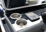 Center console of a vehicle with two stainless cup holders and a small keypad/remote control on a glossy black surface