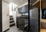 Interior of a compact modern RV kitchen with open pull-out drawers, stainless appliances, and white cabinetry along a narrow hallway area.