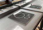 Induction cooktop with a circular heating zone and touch controls on a stainless countertop.