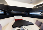 Luxurious yacht cabin lounge with a U-shaped white seating area around a dark triangular table and red and purple cushions.