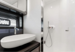 Modern bathroom with a white oval vessel sink on a dark vanity and a handheld shower inside a glass shower area.