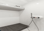 White tiled shower with a dark wood bench along the wall and a handheld showerhead on the right.