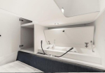 Interior of a small white boat cabin: a bed with a dark blue cushion, open cabinet doors, and a compact sink area with faucets visible above the mattress.