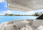 White yacht deck with L-shaped seating and a central table, blue water and palm-backed shoreline in the distance, sunny day.