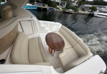 Cream leather seating surrounding a small wooden round table on a boat deck, with water and docked boats in the background.