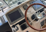 Boat cockpit with wooden steering wheel and multiple navigation screens, controls, and throttle levers on a beige dash