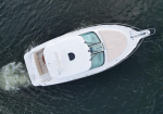 Aerial view of a white motor yacht cruising on dark-blue water, seen from above with a spacious deck and seating area at the stern.