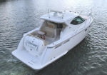 White motor yacht seen from above, cruising on calm water with open cockpit and rear seating area near a swim platform.