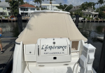 Rear view of a white motorboat with a beige canvas cover; the stern reads 'L'Espérance' and 'Fort Lauderdale, FL' with a marina and houses in the background.