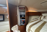 Interior of a small boat cabin with an open tall wooden storage cabinet next to the bed, exposing shelves and assorted gear inside.