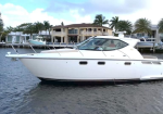 White motor yacht gliding on calm water with waterfront houses and palm trees in the background.
