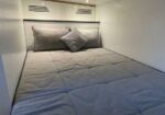 Compact cabin bed with gray quilted bedding and two pillows on a white wall-lined background.
