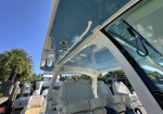 Luxurious white-leather boat cockpit with multiple captain-style seats under an open blue canopy, at a sunny marina with palm trees in the background.