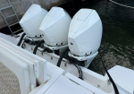 Three white outboard motors mounted on the stern of a boat at a dock, with hoses and rigging attached.