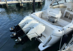 White motorboat docked at a marina with three outboard engines tilted up and calm water surrounding it.