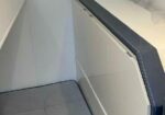 Close-up of a gray escalator handrail along a pale wall, viewed at an angle from the side.