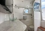 Compact boat galley with marble countertop, glass sink, and a small head (toilet) at the back; wooden deck steps on the right.