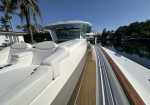 Luxurious white motor yacht docked at a marina, with tan teak deck and palm trees in a sunny waterfront setting.