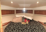 Cozy boat cabin with a large bed, black-and-white patterned comforter, beige pillows, and a stuffed animal on a small, enclosed space with wooden cabinets above.