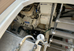 Interior of a utility compartment showing electrical control boxes, pumps, and tangled wiring, with metal stairs on the right and multiple hoses connected at the bottom for the system.