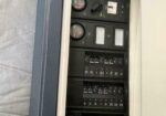 Open electrical service panel with multiple circuit breakers and round gauges visible inside a wall-mounted cabinet.