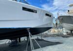 Two large yachts on stands in a dry-dock area, scaffolding around them for maintenance under a blue sky.