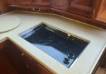 Built-in black glass electric cooktop set into a speckled beige countertop with wooden cabinets above and below.