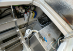 Open storage compartment on a boat showing cleaning supplies, bottles, and a crate on a shelf under the stairs.