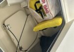 Inside a small boat/storage area: a yellow flotation device sits next to a white hatch and tangled cables.