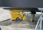Underside of a boat hull resting on a yellow padded cradle and trailer on a paved surface.
