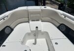 White boat bow with curved beige cushioned seating, central pedestal post, and built-in storage compartments; dock and water in background.