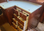 Boat galley with multiple wooden drawers open, showing white interior drawers and items inside beneath a light countertop.