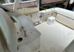 White boat cockpit with cushioned seating, built‑in storage, and a yellow cord running to a dockside power source; a white cooler labeled 'Lady Jane' sits on the deck.